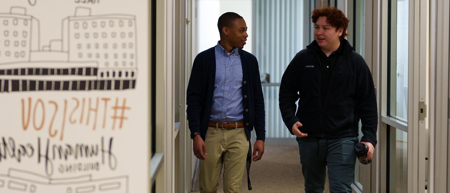 Two young men walk together down a hallway in a building on O U's campus.